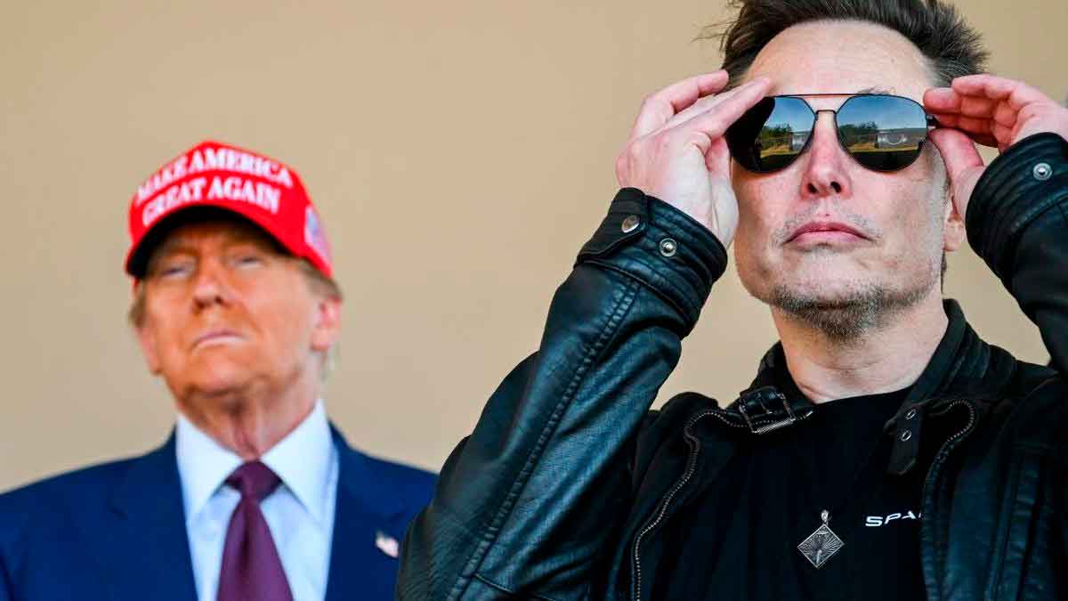 Primer plano de Elon Musk con chaqueta oscura y gafas de sol mientras, al fondo está Trump con una gorra con un mensaje propagandístico