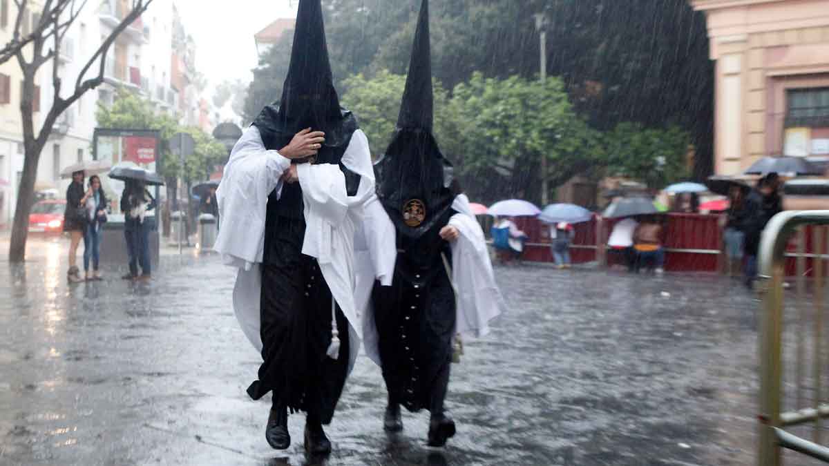 Dos nazarenos con capirotes negros caminan bajo la lluvia en la Semana Santa de Andalucía