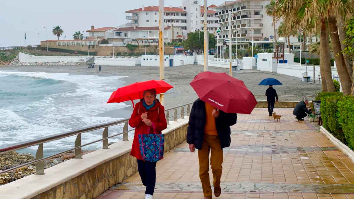 Personas paseando con paraguas bajo la lluvia junto al mar durante el puente de mayo