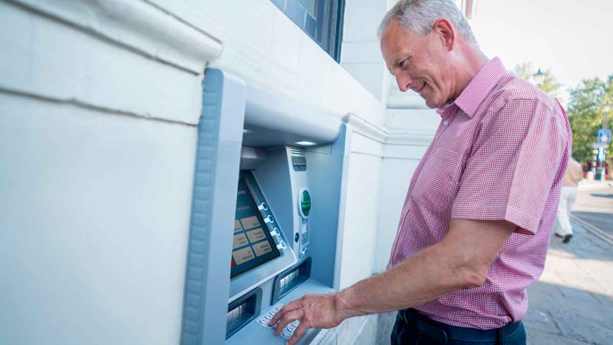 Hombre mayor retirando efectivo en un cajero automático, fechas de cobro de las pensiones en abril de 2025