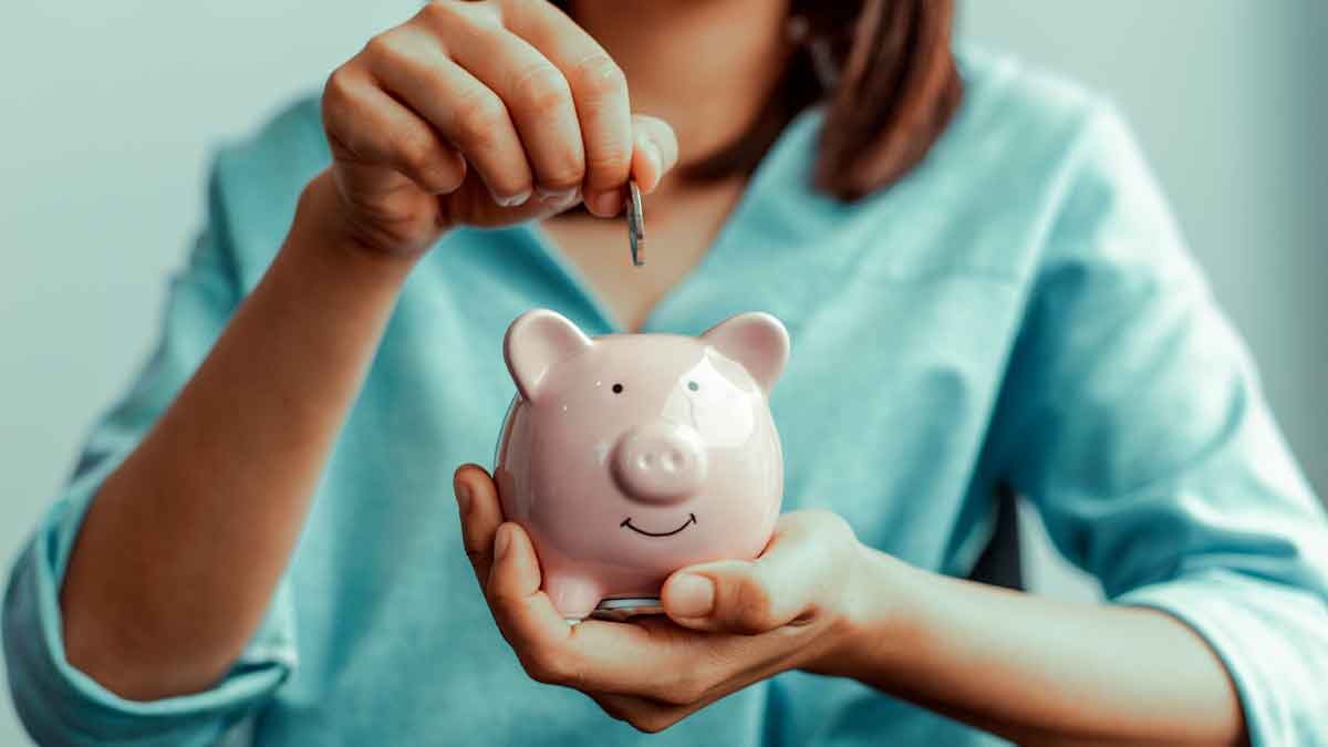 Mujer depositando una moneda en una hucha rosada para ilustrar el método 50/30/20 de ahorro según tu sueldo