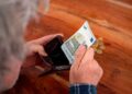 Persona mayor revisando su cartera con un billete de 5 euros, simbolizando la compatibilidad de la pensión de viudedad y la jubilación