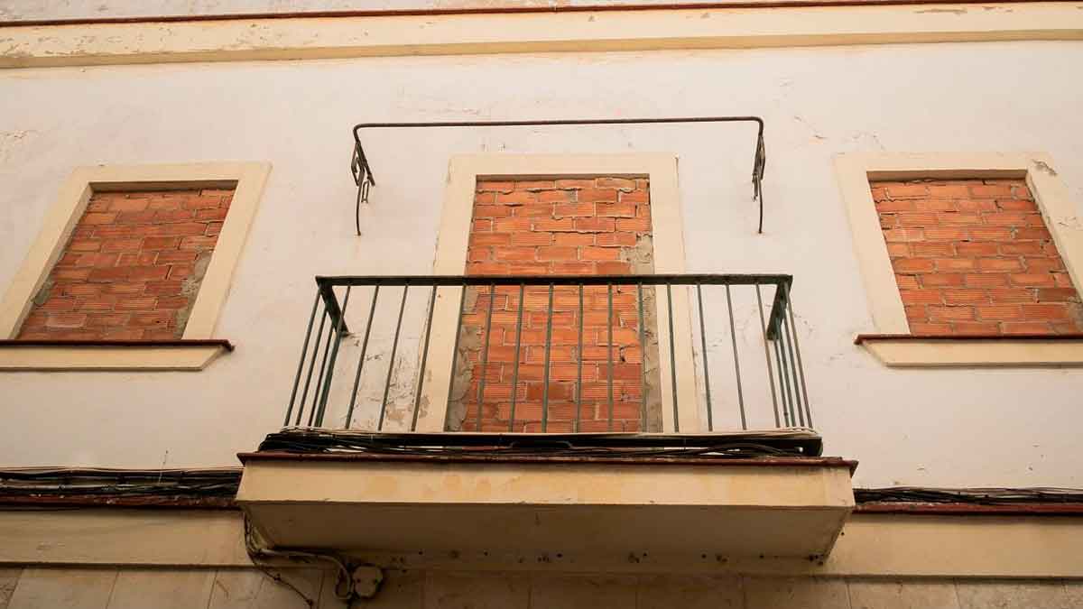 Fachada de vivienda vacía con ventanas tapiadas y balcón sin uso, ejemplo del coste anual de más de 3.000 €