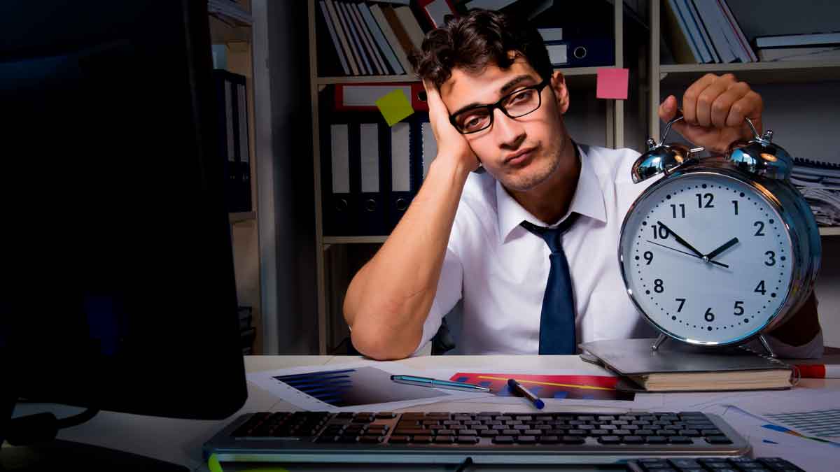 Trabajador de oficina cansado sostiene un gran reloj despertador, reflejando la necesidad de cambiar el horario laboral para conciliar
