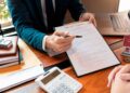 Asesor financiero muestra contrato de préstamo hipotecario y calculadora mientras explica TIN y TAE al cliente