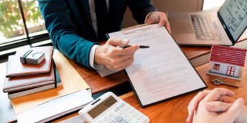 Asesor financiero muestra contrato de préstamo hipotecario y calculadora mientras explica TIN y TAE al cliente