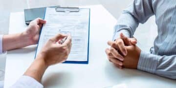 Trabajador del INSS muestra al solicitante un formulario de revisión de la pensión por incapacidad permanente.