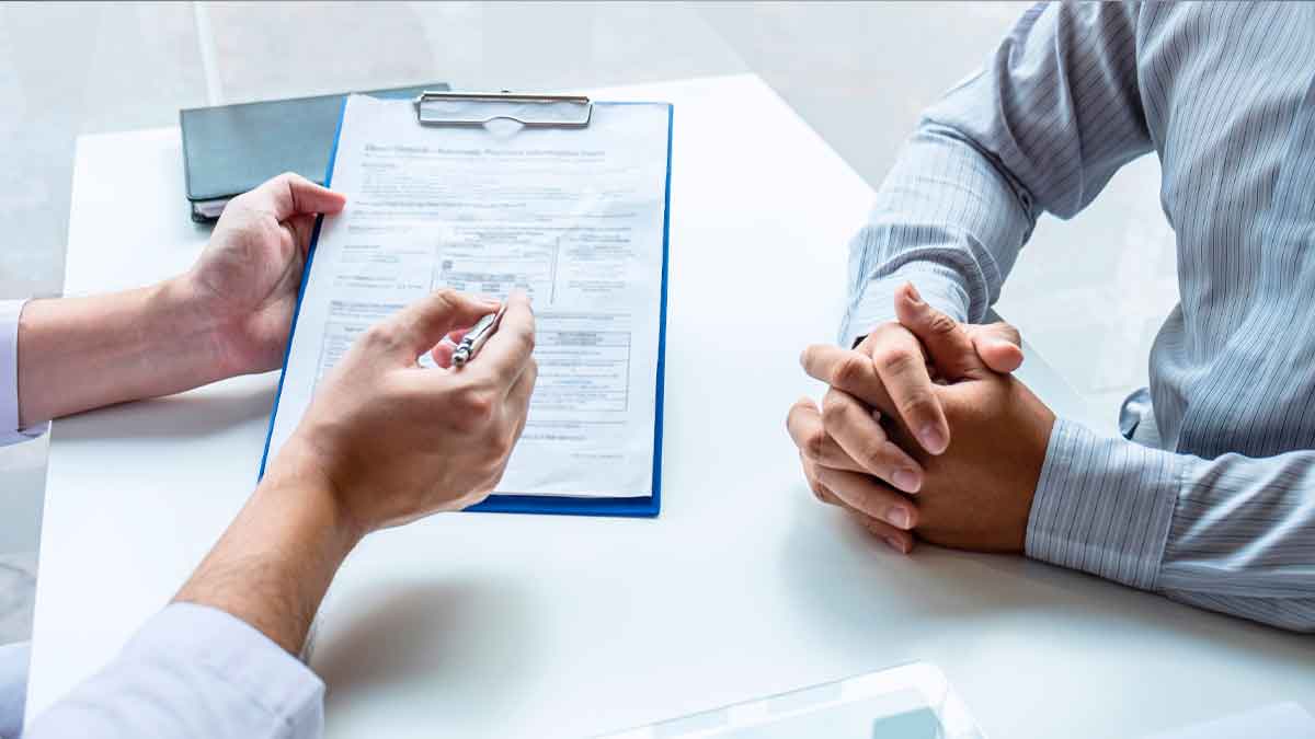 Trabajador del INSS muestra al solicitante un formulario de revisión de la pensión por incapacidad permanente.