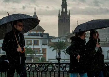 Peatones con paraguas en Sevilla bajo chubascos; la Giralda al fondo, alerta de AEMET en Andalucía