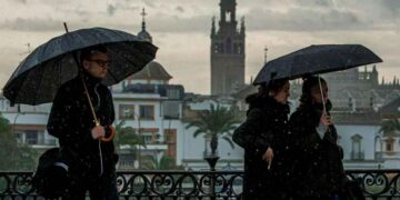 Peatones con paraguas en Sevilla bajo chubascos; la Giralda al fondo, alerta de AEMET en Andalucía