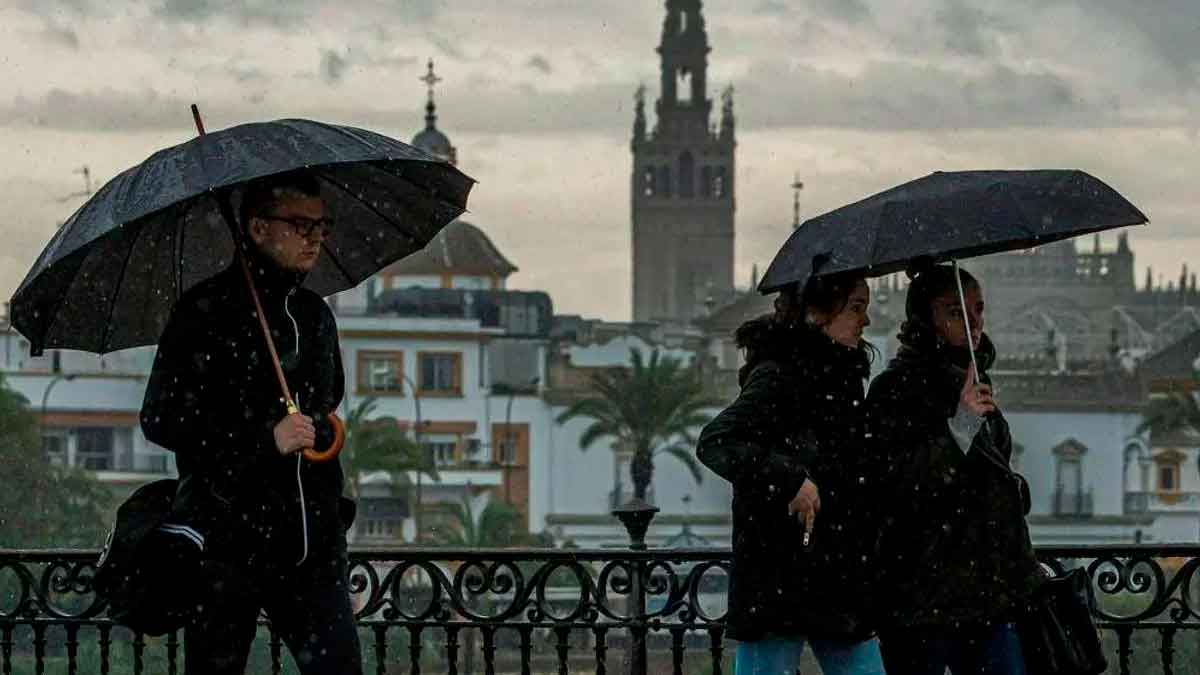 Peatones con paraguas en Sevilla bajo chubascos; la Giralda al fondo, alerta de AEMET en Andalucía