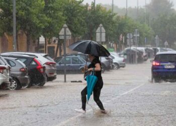 Mujer con paraguas cruza una calle inundada en Andalucía durante las intensas tormentas y granizo alertadas por la AEMET el 14 de mayo de 2025