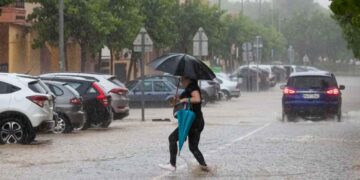 Mujer con paraguas cruza una calle inundada en Andalucía durante las intensas tormentas y granizo alertadas por la AEMET el 14 de mayo de 2025