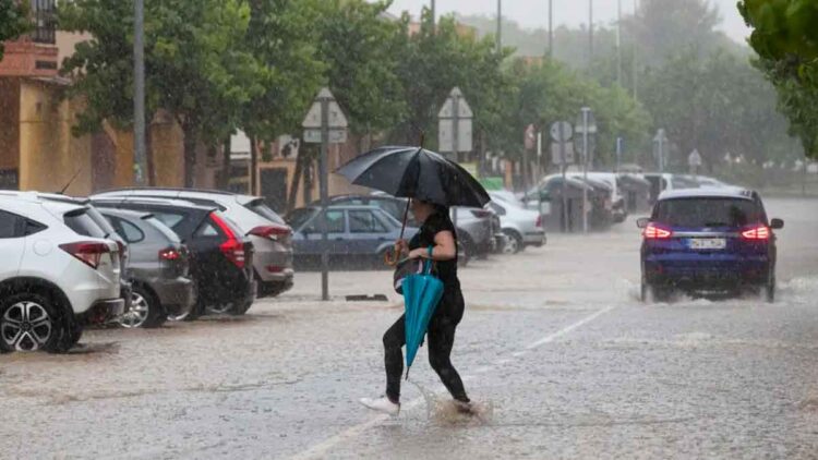 Mujer con paraguas cruza una calle inundada en Andalucía durante las intensas tormentas y granizo alertadas por la AEMET el 14 de mayo de 2025