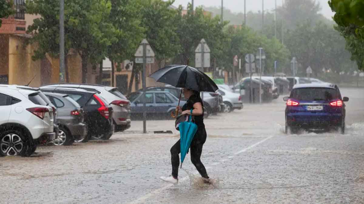 Mujer con paraguas cruza una calle inundada en Andalucía durante las intensas tormentas y granizo alertadas por la AEMET el 14 de mayo de 2025