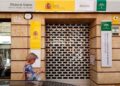 Mujer frente a una oficina cerrada del SEPE consultando su teléfono móvil