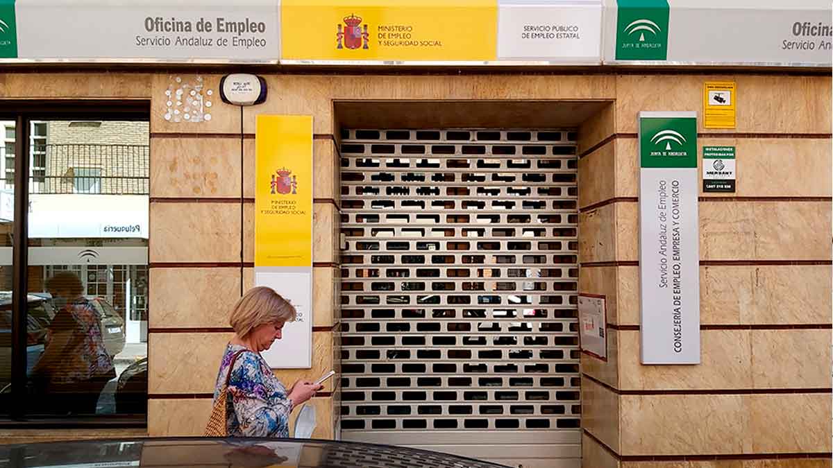 Mujer frente a una oficina cerrada del SEPE consultando su teléfono móvil