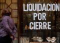 Cartel de “Liquidación por cierre” en el escaparate de un comercio andaluz mientras una mujer observa la vitrina
