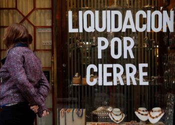 Cartel de “Liquidación por cierre” en el escaparate de un comercio andaluz mientras una mujer observa la vitrina