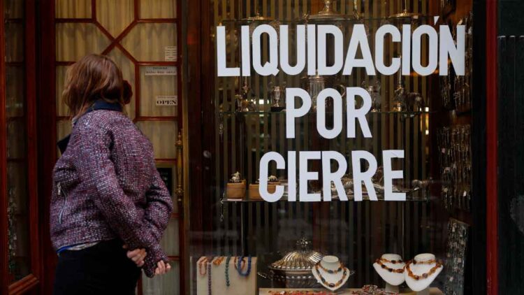 Cartel de “Liquidación por cierre” en el escaparate de un comercio andaluz mientras una mujer observa la vitrina