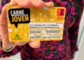 Carné Joven Andalucía tarjeta amarilla con descuentos, sostenida por una joven ante fondo colorido