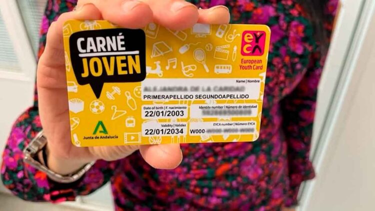 Carné Joven Andalucía tarjeta amarilla con descuentos, sostenida por una joven ante fondo colorido
