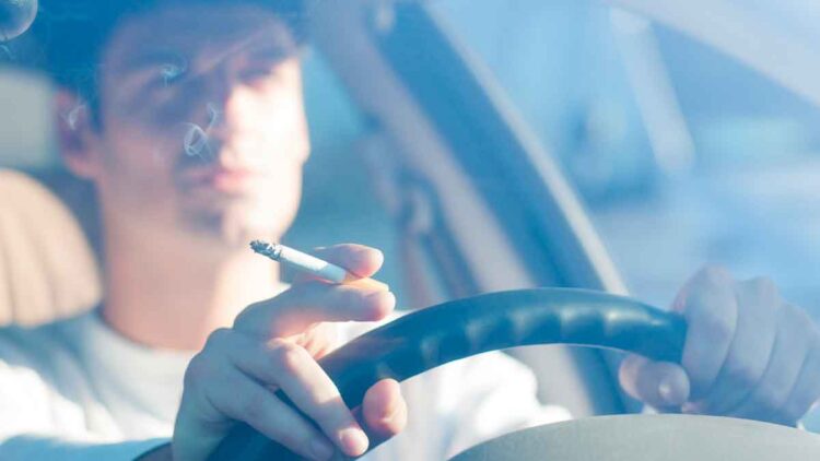 Conductor fumando un cigarrillo al volante, posible multa DGT por distracción y colillas