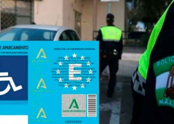 Tarjeta de aparcamiento para personas con movilidad reducida de la Junta de Andalucía sobre el capó de un coche con Policía Local al fondo