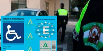 Tarjeta de aparcamiento para personas con movilidad reducida de la Junta de Andalucía sobre el capó de un coche con Policía Local al fondo