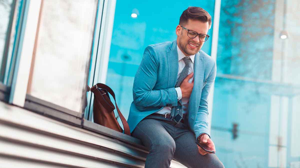 Trabajador con traje sujeta su pecho por dolor cardíaco frente a una oficina, posible infarto vinculado al estrés laboral