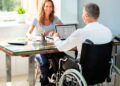 Persona en silla de ruedas trabajando en oficina con una compañera, representando inclusión laboral en Andalucía