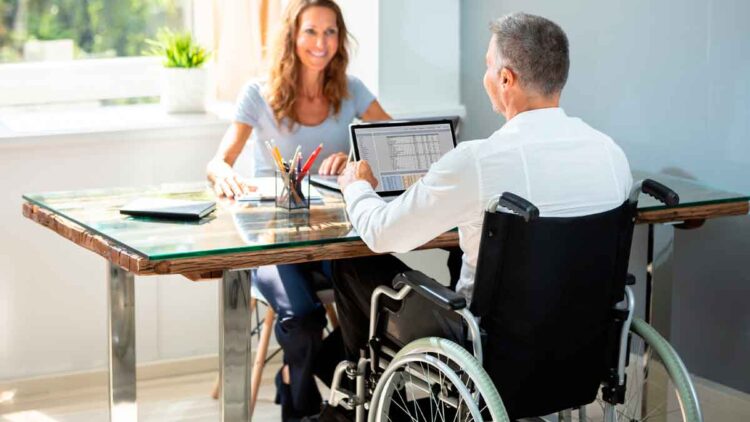 Persona en silla de ruedas trabajando en oficina con una compañera, representando inclusión laboral en Andalucía