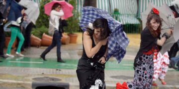 Mujeres con traje de flamenca sujetan paraguas volteados por viento y lluvia durante chubascos en Andalucía (7-5-2025)