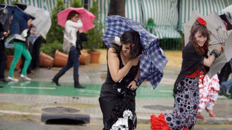 Mujeres con traje de flamenca sujetan paraguas volteados por viento y lluvia durante chubascos en Andalucía (7-5-2025)