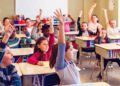 Niños y niñas levantando la mano en clase, ejemplo de alumnado que puede beneficiarse de las becas 2025/26 de apoyo educativo