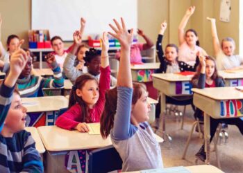 Niños y niñas levantando la mano en clase, ejemplo de alumnado que puede beneficiarse de las becas 2025/26 de apoyo educativo