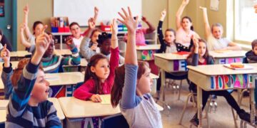 Niños y niñas levantando la mano en clase, ejemplo de alumnado que puede beneficiarse de las becas 2025/26 de apoyo educativo