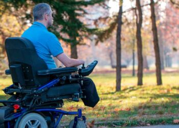 Hombre con discapacidad en silla de ruedas eléctrica pasea por un parque otoñal, ilustrando la nueva pensión no contributiva de incapacidad publicada en el BOE para 2025