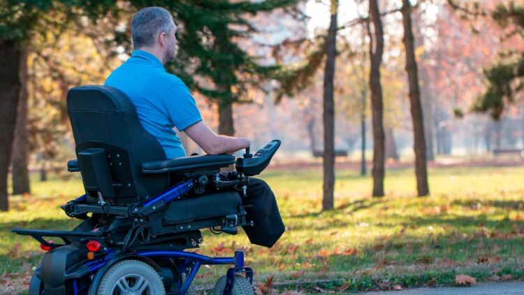 Hombre con discapacidad en silla de ruedas eléctrica pasea por un parque otoñal, ilustrando la nueva pensión no contributiva de incapacidad publicada en el BOE para 2025