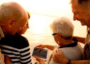Grupo de jubilados consultando una tablet al atardecer junto al mar sobre la pensión máxima en Europa, EE. UU. y Canadá