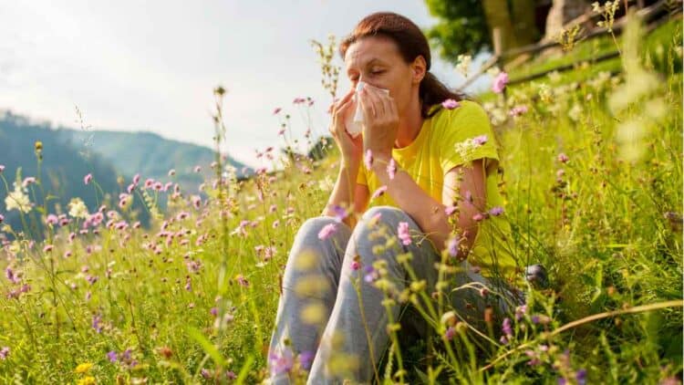 Mujer con alergia en primavera sentada en un campo lleno de flores y polen