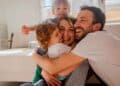 Padres sonrientes abrazando a sus dos hijos en el salón, símbolo de la conciliación familiar lograda con la reducción de jornada laboral