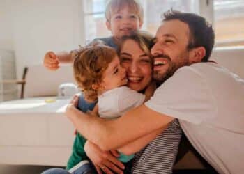 Padres sonrientes abrazando a sus dos hijos en el salón, símbolo de la conciliación familiar lograda con la reducción de jornada laboral