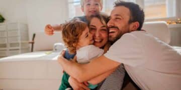 Padres sonrientes abrazando a sus dos hijos en el salón, símbolo de la conciliación familiar lograda con la reducción de jornada laboral