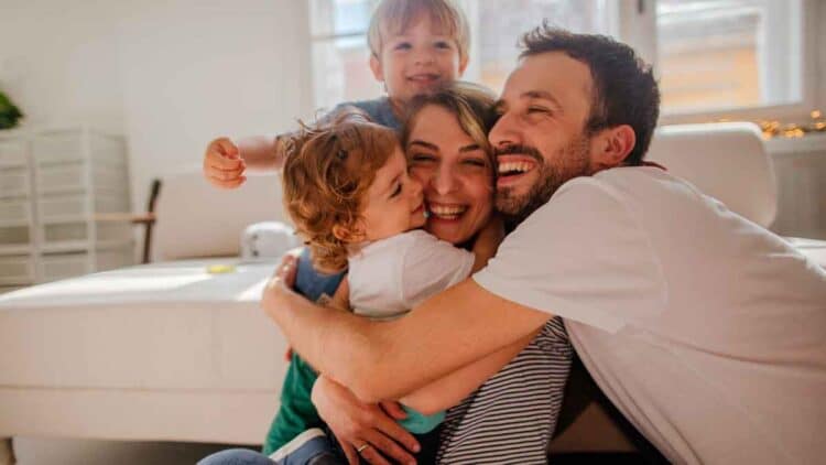 Padres sonrientes abrazando a sus dos hijos en el salón, símbolo de la conciliación familiar lograda con la reducción de jornada laboral