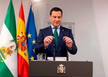 El presidente del Gobierno andaluz anuncia la ayuda de hasta 1.449 € mensuales con banderas de Andalucía, España y UE detrás.