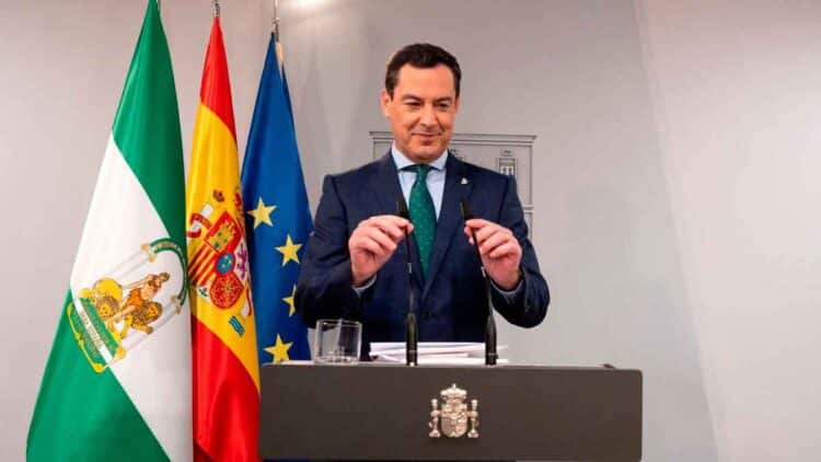 El presidente del Gobierno andaluz anuncia la ayuda de hasta 1.449 € mensuales con banderas de Andalucía, España y UE detrás.