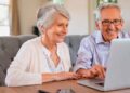 Pareja de personas mayores solicita online la pensión de jubilación 2025 en un portátil, revisando la documentación necesaria