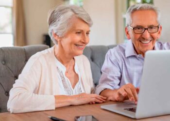 Pareja de personas mayores solicita online la pensión de jubilación 2025 en un portátil, revisando la documentación necesaria