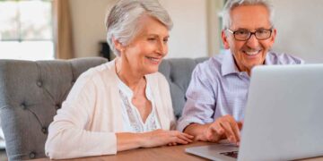 Pareja de personas mayores solicita online la pensión de jubilación 2025 en un portátil, revisando la documentación necesaria
